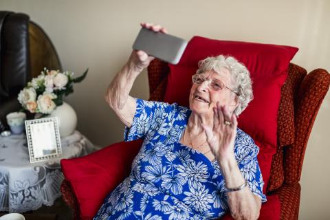 An older women sits in an armchair and makes a video call.