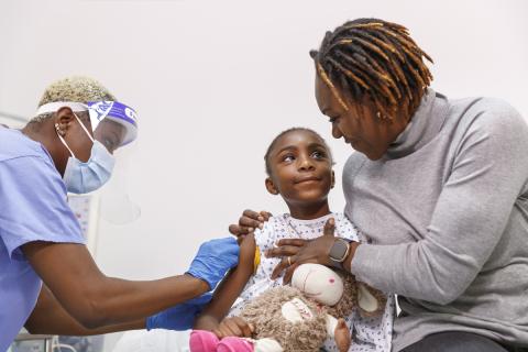 A Medicaid eligible child receives a Covid-19 vaccine while her mother looks on