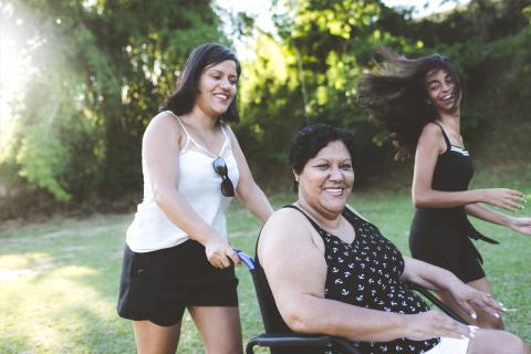 Middle-aged mother is pushed in wheelchair by her two daughters.