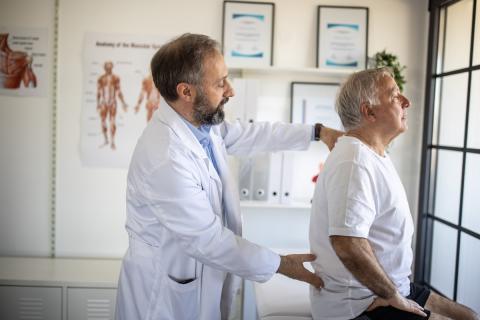 A physician elevates his older male patient's complaint of back pain