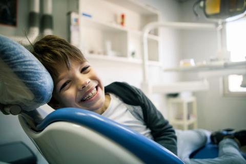 A young boy who has been referred to a dentist smiles from a dental exam chair