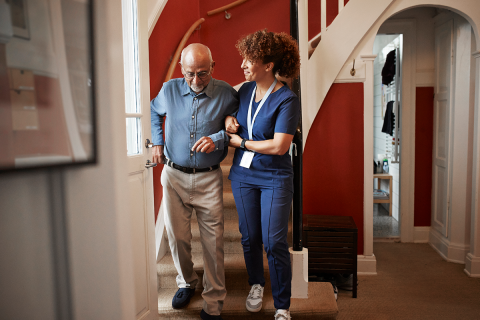 A woman helping an older man walk down the stairs. 
