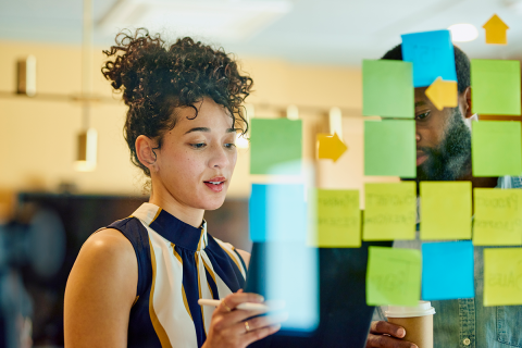 A woman and a man overlooking a board of sticky notes. 