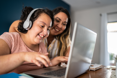 A person with IDD who has a headset on with her mother working on a laptop. 