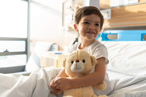 A young boy holding a teddy bear while in a hospital bed.